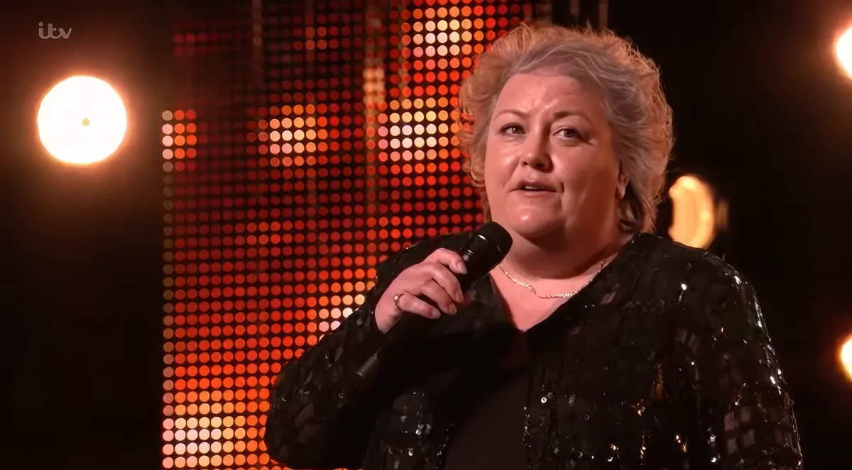 A woman in a black sequined outfit holds a microphone, standing in front of a vibrant, illuminated background.
