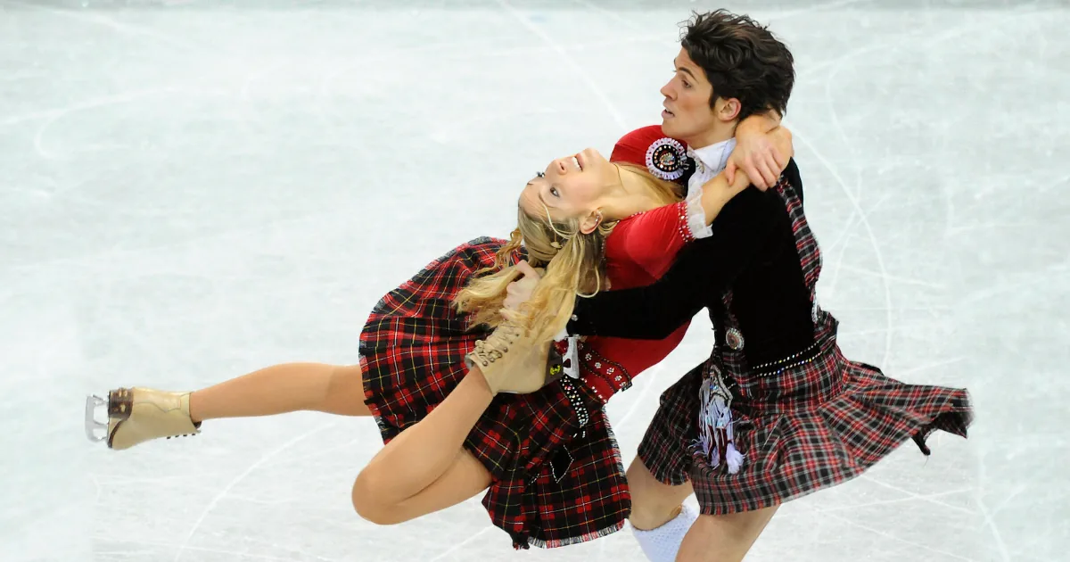 A couple in plaid costumes performs a synchronized ice skating move on the rink.