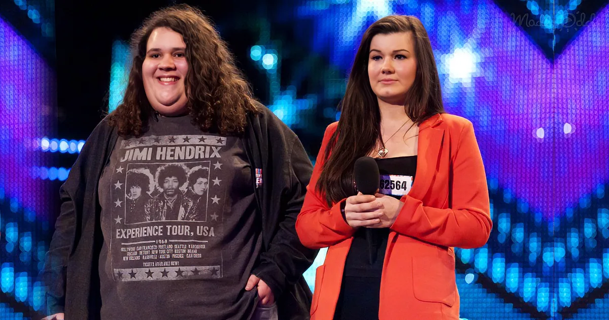 A person in a Jimi Hendrix shirt stands next to another person in an orange blazer holding a microphone.
