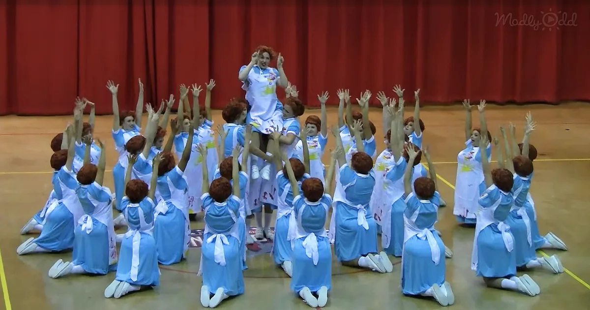 A woman in a blue dress is being lifted by a group of people in matching outfits in a gymnasium.