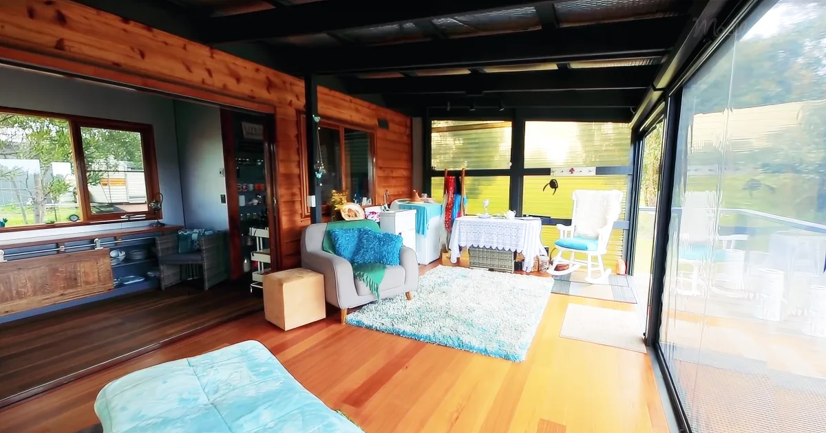 A cozy living space with wooden floors, a gray armchair, a white rocking chair, and a large window offering a view of...