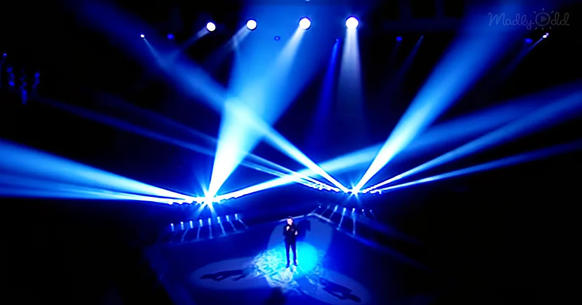 A person stands on a stage bathed in blue light, surrounded by bright beams of light.