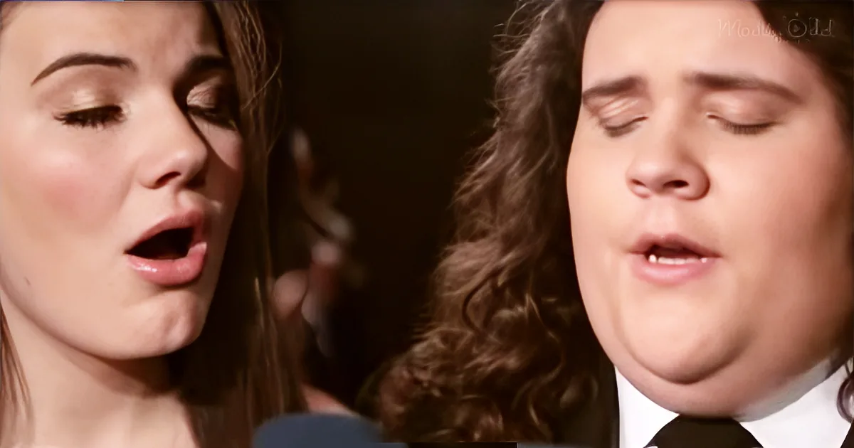 A woman and a man with long hair are singing with their eyes closed, appearing deeply engaged.