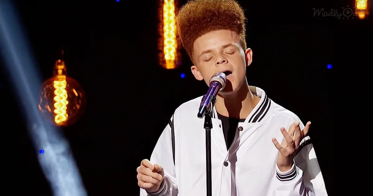 A young person in a white jacket sings passionately into a microphone on stage with glowing lights.