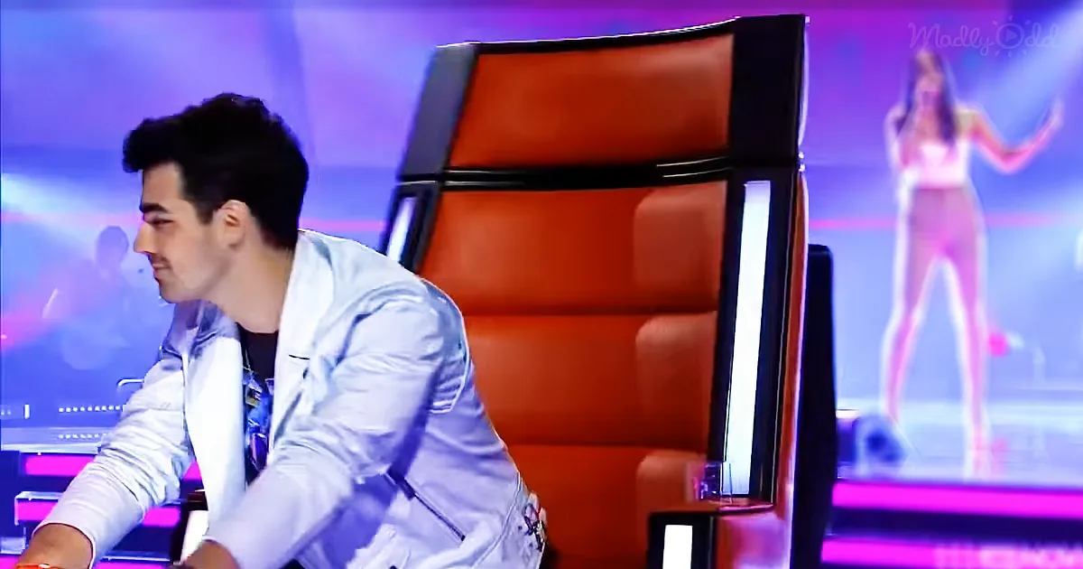 A man in a white shirt leans forward, looking at a stage with a singer in a white outfit.