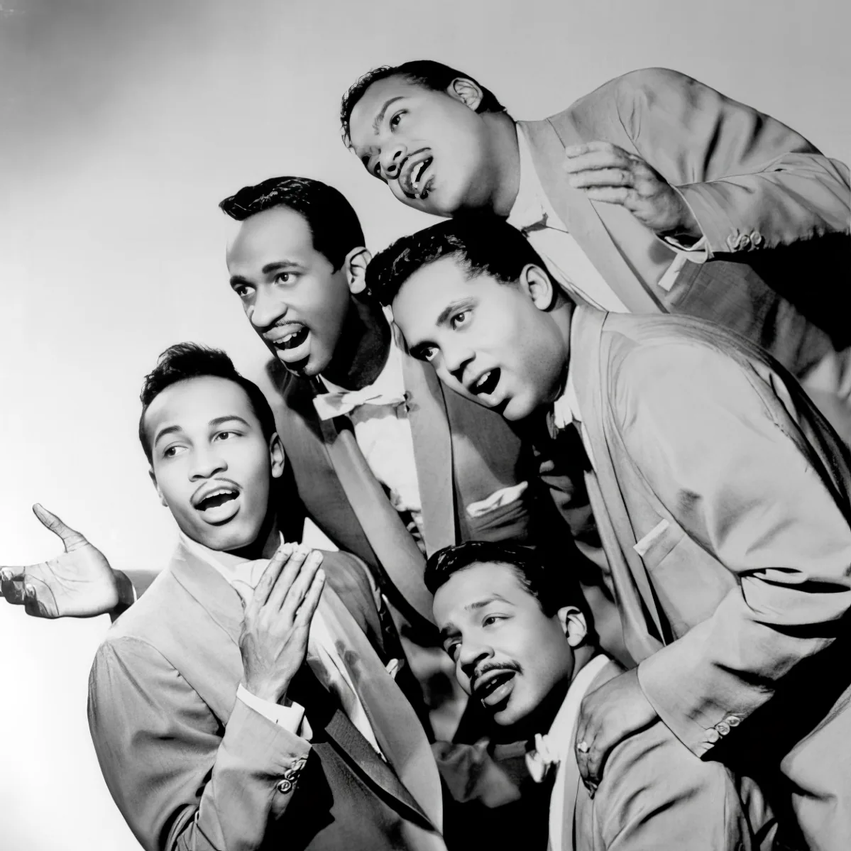 A group of five men in suits, singing and posing together in a vintage style.