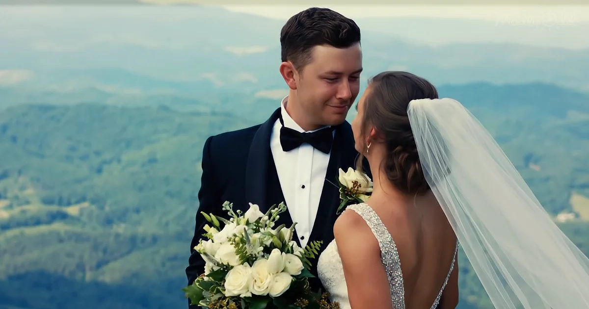 A bride and groom share a tender moment, the bride holding a bouquet, against a scenic mountain backdrop.