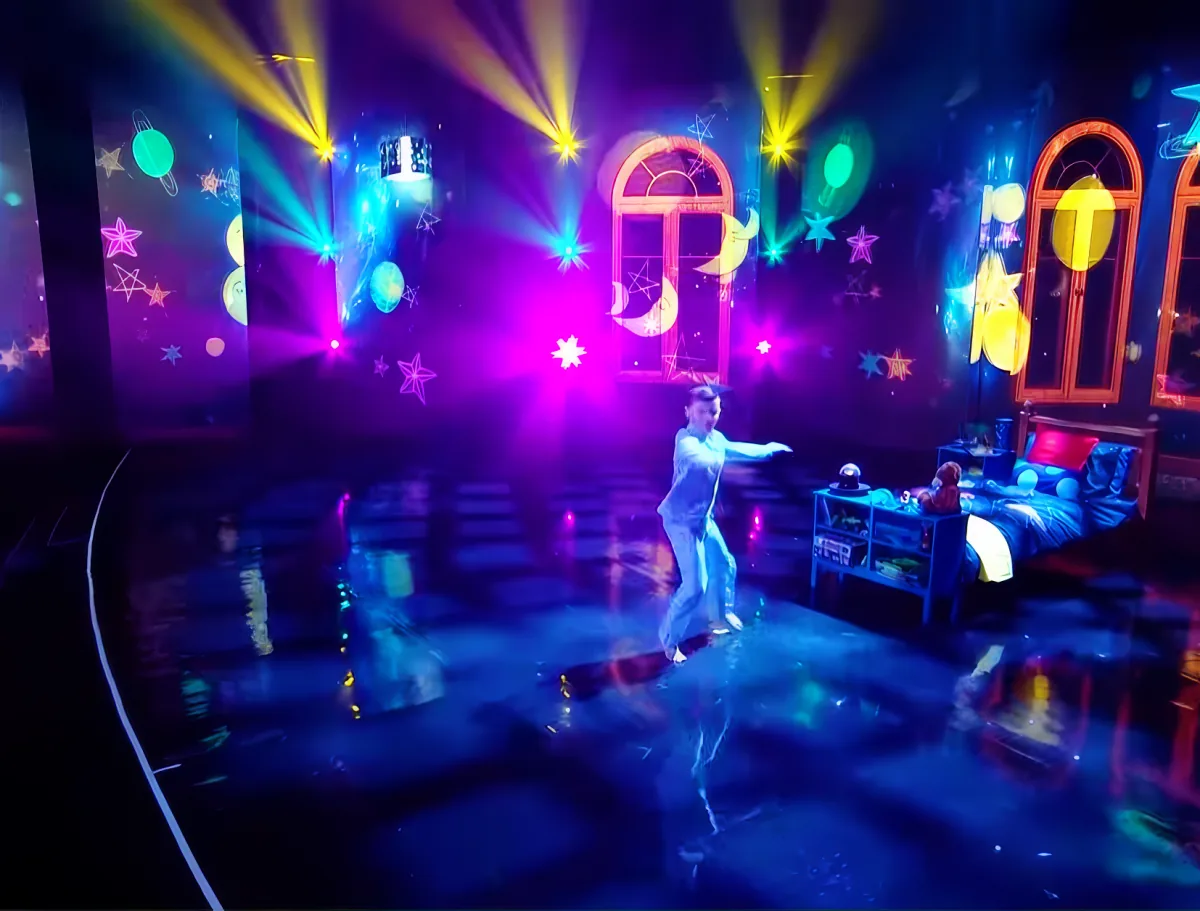 A person dances in a colorful, starry room with a bed and shelves.