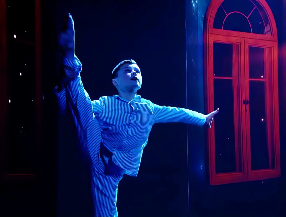 A person in a striped shirt is performing a dance move with arms outstretched, illuminated by blue and red lighting.