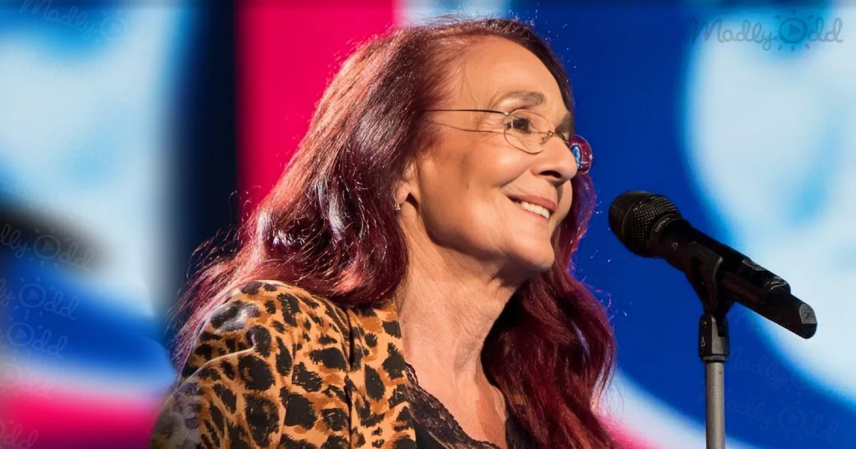 A woman with long, reddish-brown hair smiles while wearing a leopard print top, standing near a microphone.