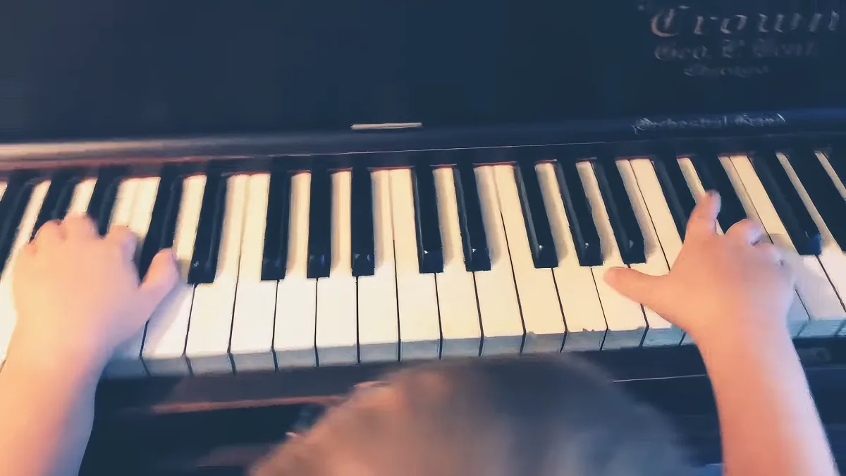 A child plays piano, hands on keys, close-up view.