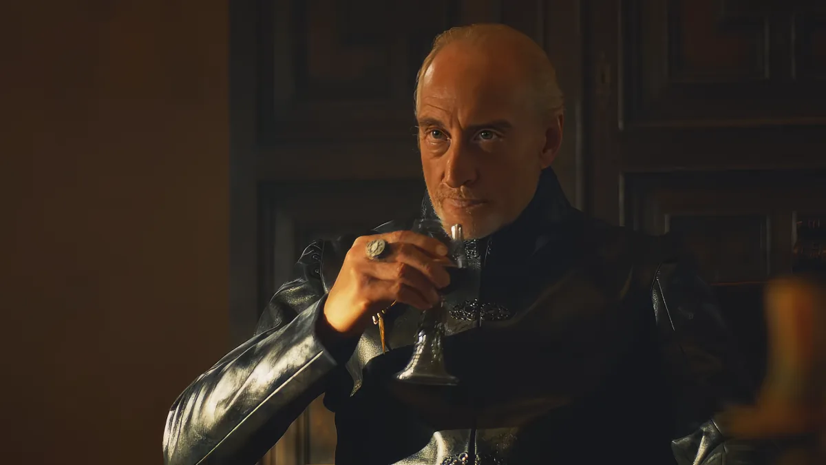 A man in dark armor holds a small object, possibly a ring, in a dimly lit room.