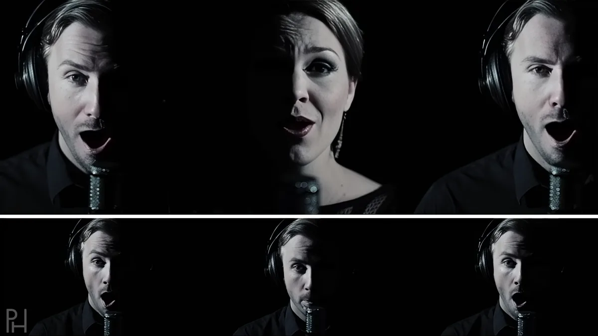 A man in a black shirt sings into a microphone, wearing headphones, with a woman in the background.