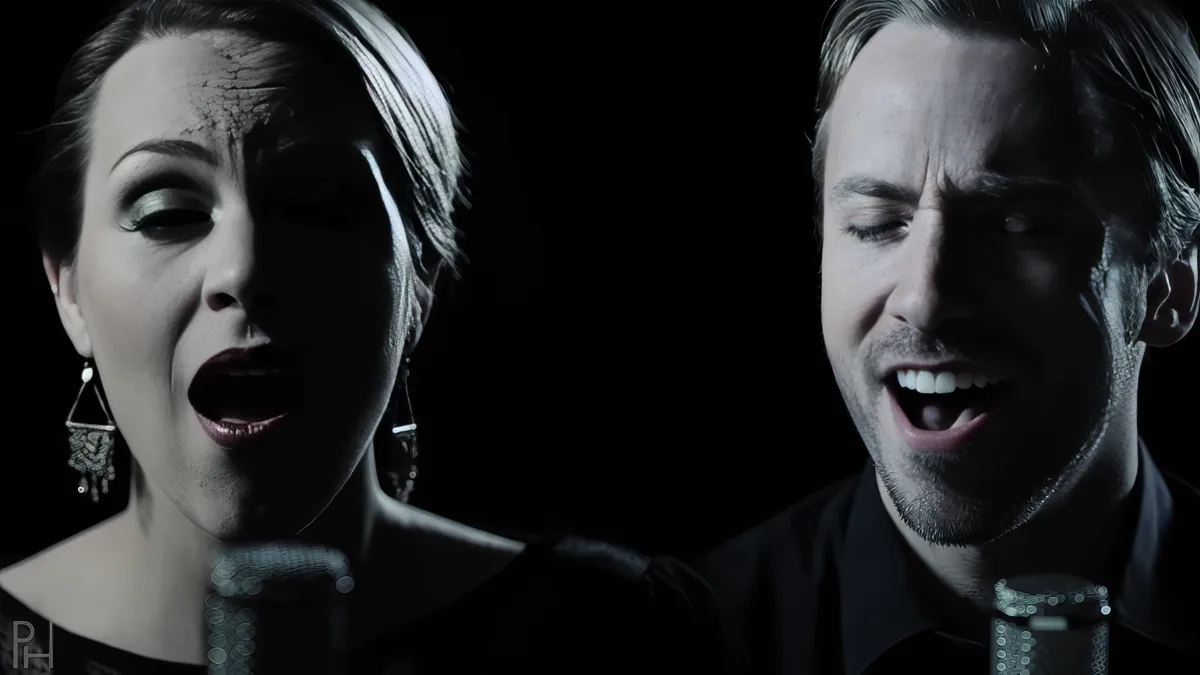 A woman and a man sing into microphones against a dark background.