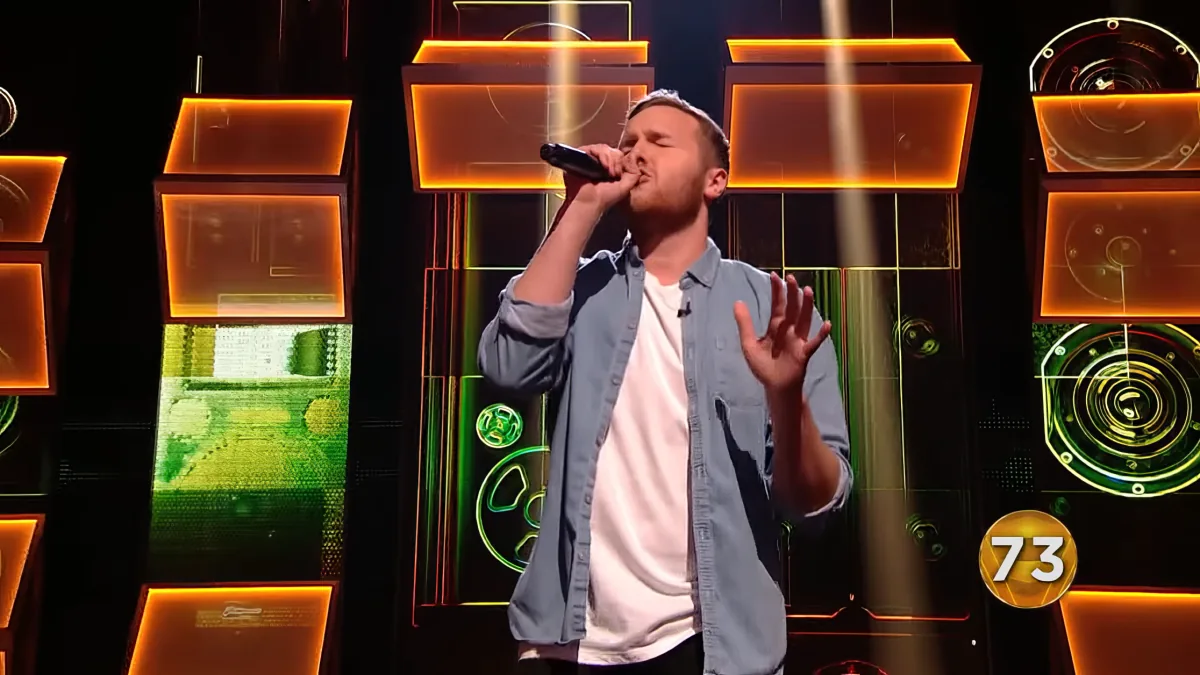 A man sings passionately on stage with a microphone, surrounded by vibrant orange and green lights.