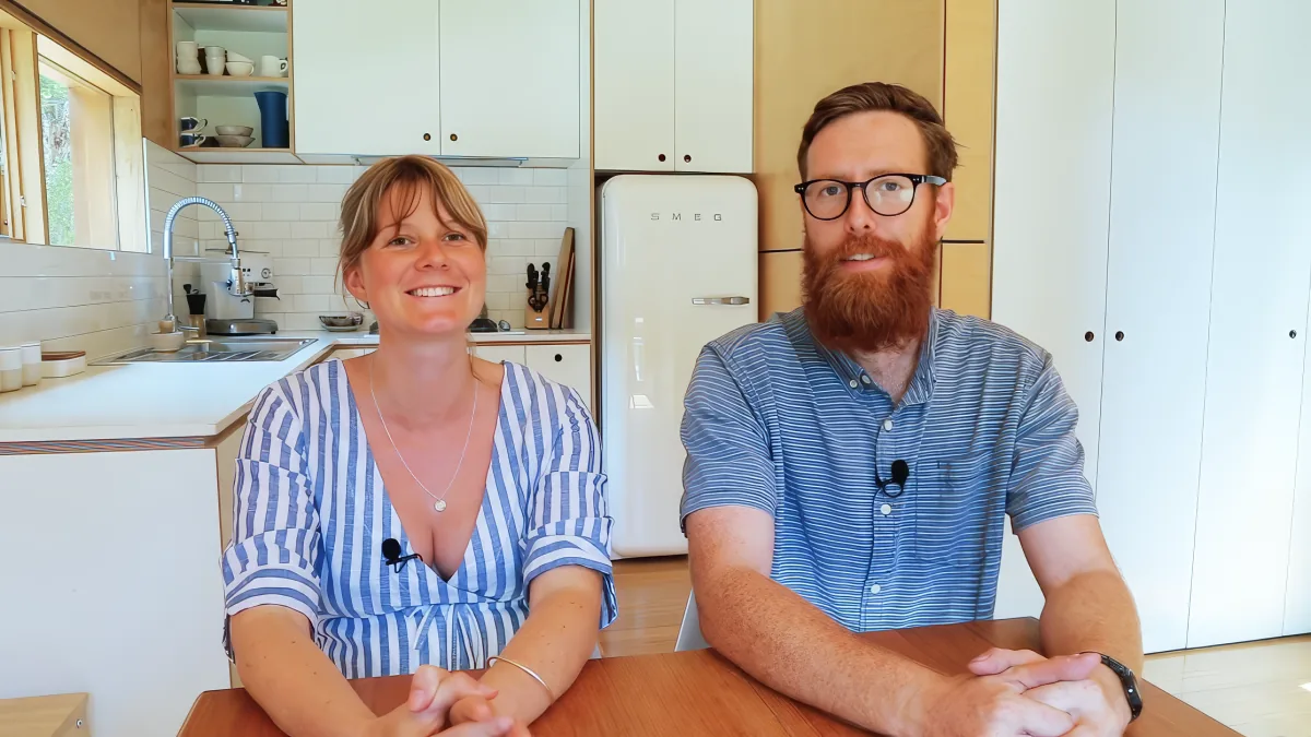 A man and woman in blue striped shirts sit at a table in a bright kitchen with white cabinets and a retro SMEG refrigerator.