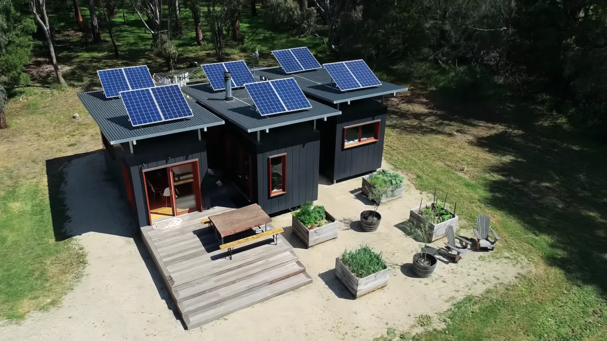 A modern house with solar panels on the roof, surrounded by a garden with wooden planters and outdoor seating.