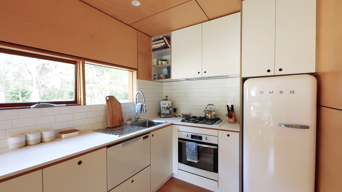 A modern kitchen with white cabinets, a SMEG refrigerator, and a window offering a view of trees.