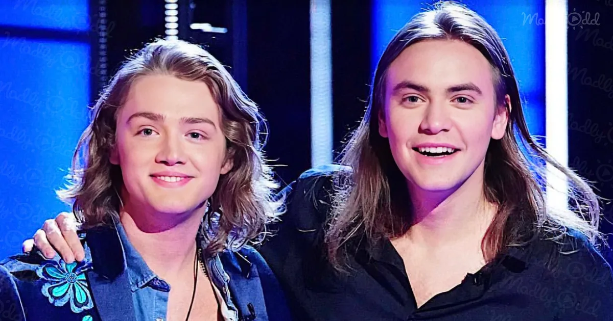 Two individuals with long hair, one in denim jacket, the other in black shirt, standing close together.