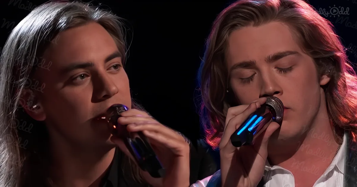 Two individuals are singing into microphones, one with long gray hair and the other with reddish-brown hair.