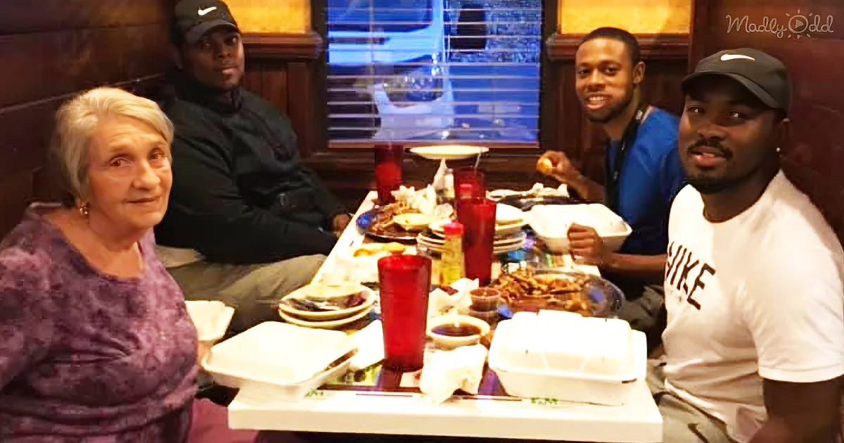 An elderly woman sits at a table with four men, enjoying a meal together in a restaurant.