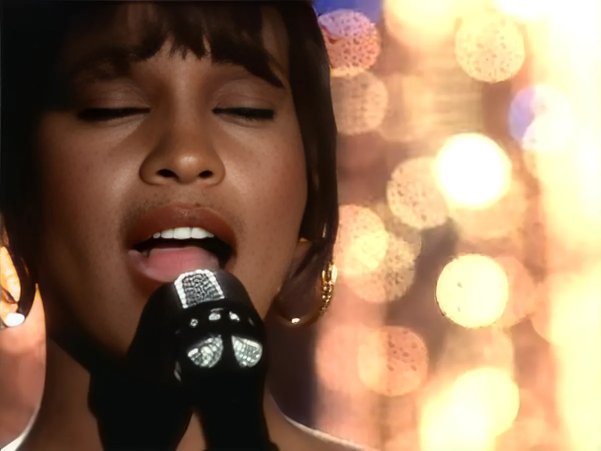 A person singing into a microphone with a blurred background of lights.