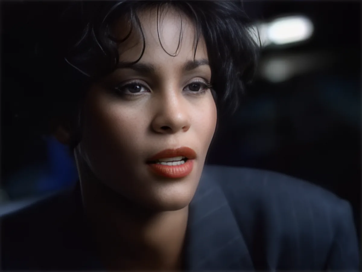 A woman with short dark hair and red lipstick is shown in close-up, wearing a dark suit.