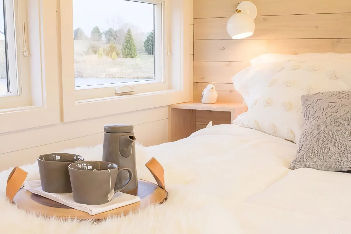 A cozy bedroom scene with a bed, a tray of mugs and a teapot, a window showing a scenic view, and a soft, inviting ambiance.