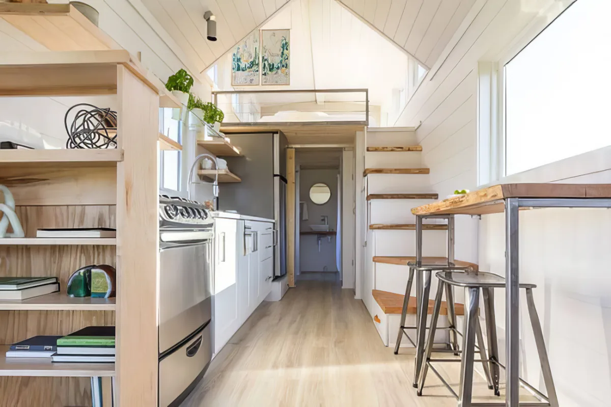 A cozy, compact kitchen with wooden shelves, a sink, and a small dining area in a tiny house.