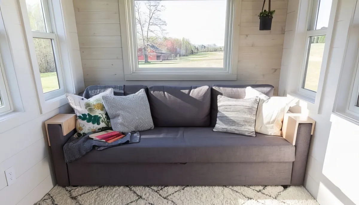 A cozy living space with a gray sofa, patterned rug, and large windows showing a scenic view.