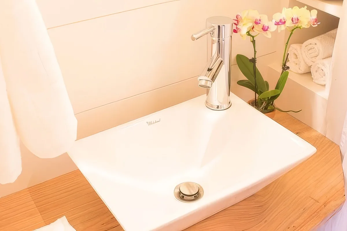 A pristine white sink with a sleek faucet sits on a wooden countertop, adorned with a delicate orchid and neatly folded...