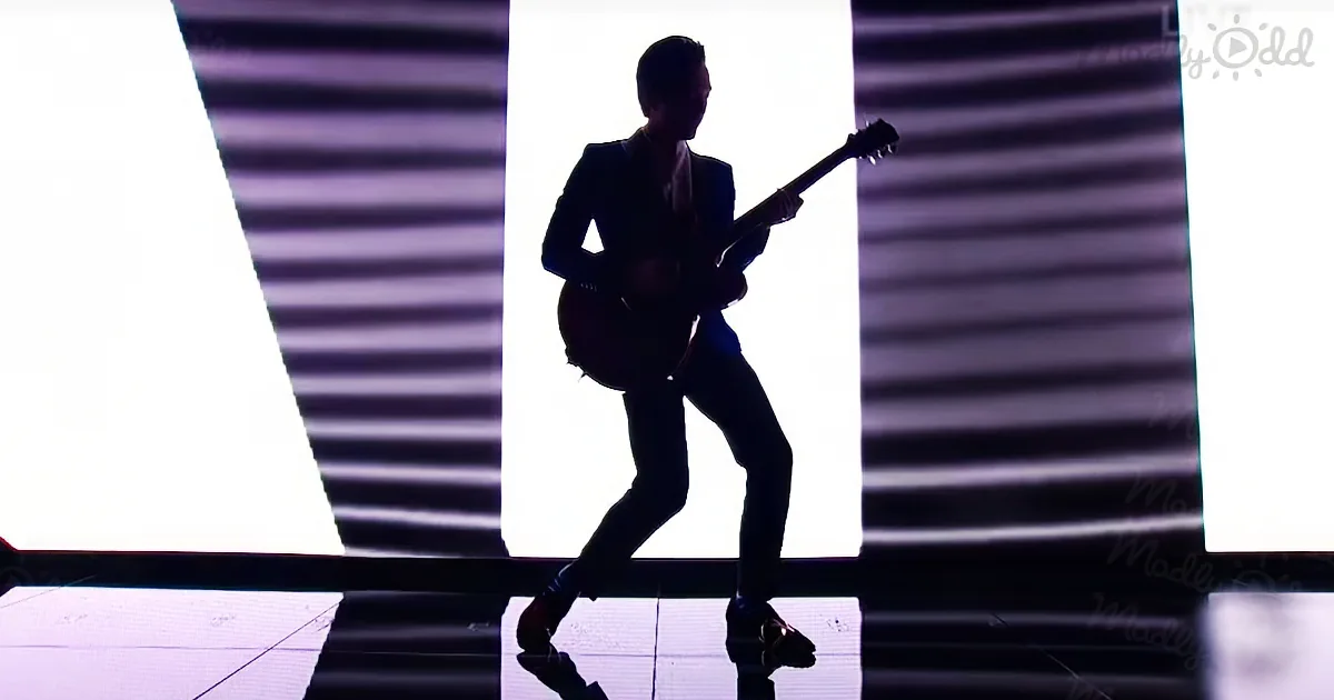 A silhouette of a person playing a guitar on stage against a striped light background.