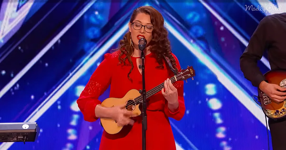 A woman in a red dress plays a ukulele on stage, singing into a microphone.