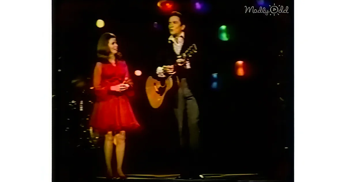 A man in a suit plays guitar while a woman in a red dress sings on stage.