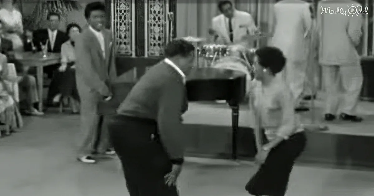A man in a suit is dancing with another man in a white shirt and dark pants.