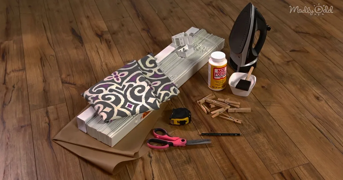 A DIY project setup includes fabric, Mod Podge, scissors, clothespins, and an iron on a wooden floor.
