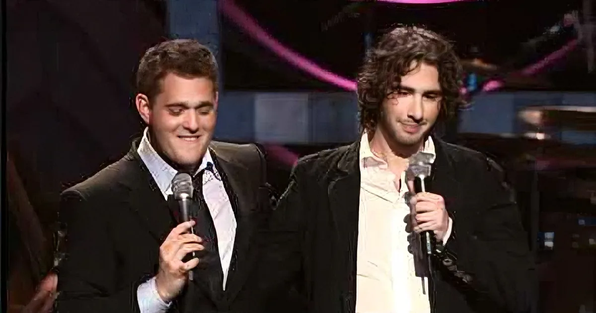 Two men in suits hold microphones on stage, smiling and speaking.