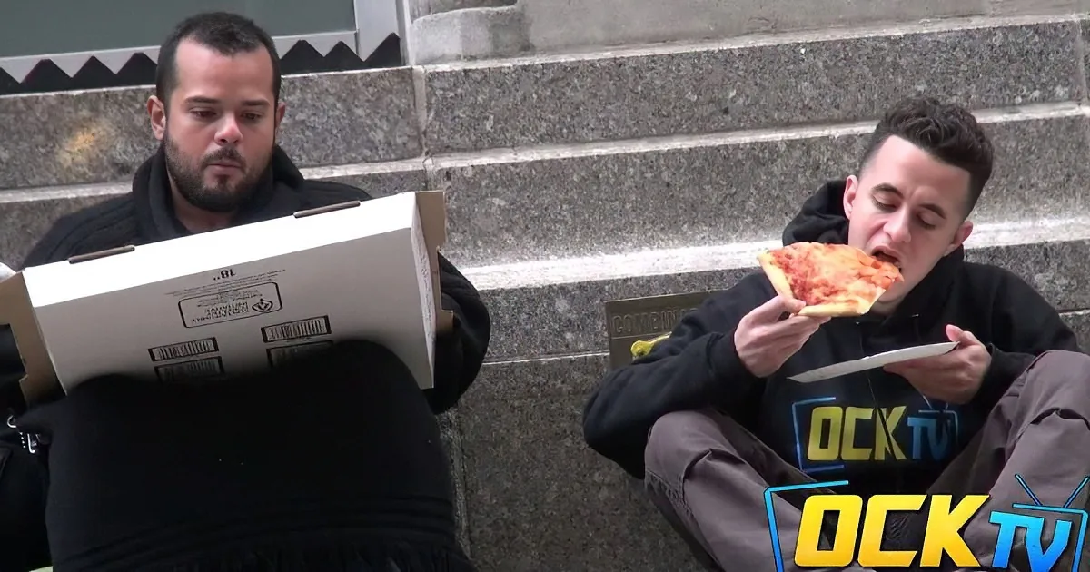Two men sit on steps, one eating pizza, the other holding a pizza box.