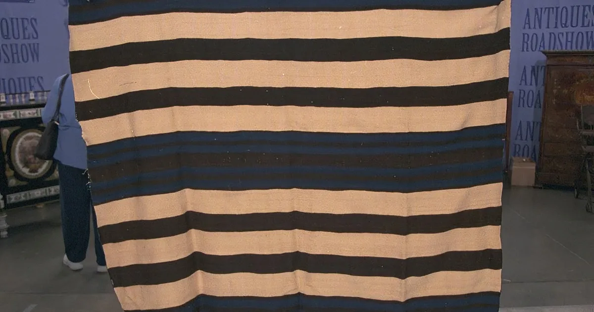 A striped blanket with alternating black and beige stripes is displayed in an Antiques Roadshow setting.