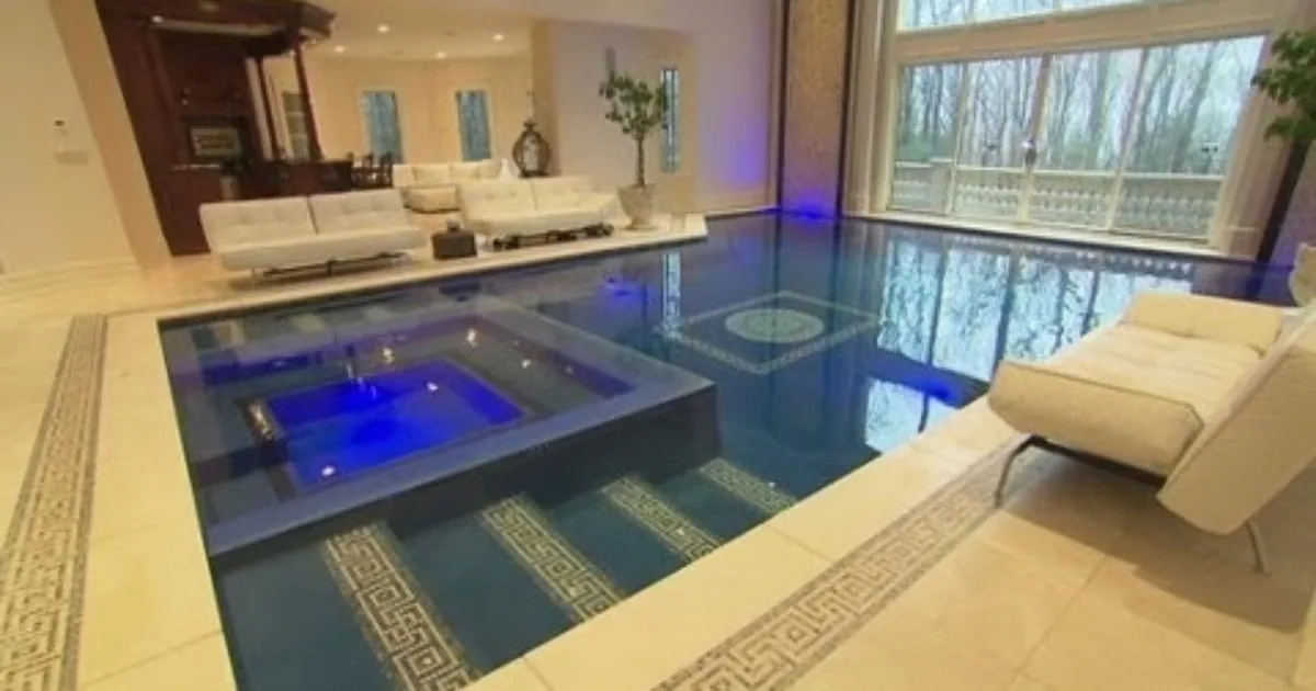 An indoor pool with a hot tub, surrounded by white furniture and large windows.