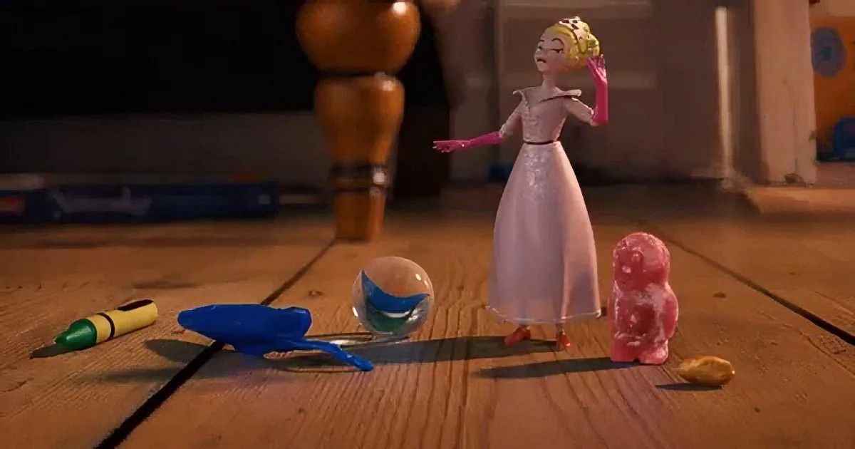 A princess doll in a pink dress stands on a wooden floor surrounded by toys and a small pink bear.
