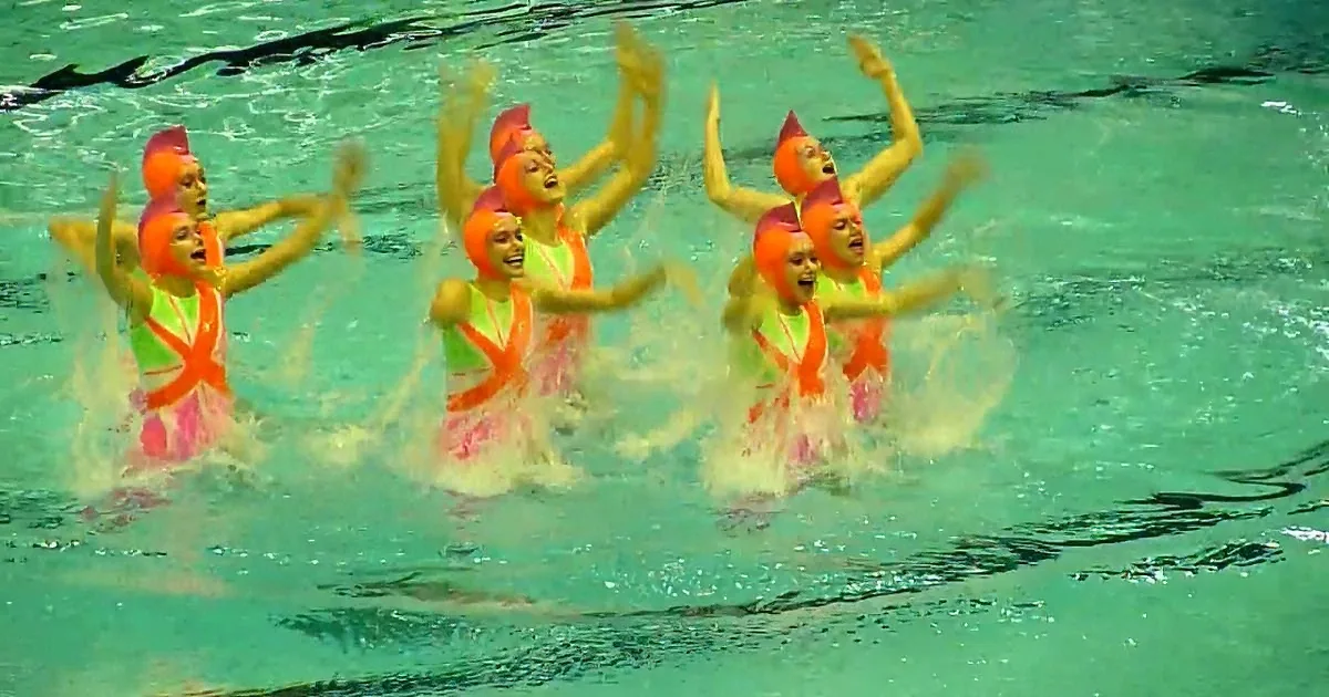 A synchronized swimming team in vibrant costumes performs a choreographed routine in a pool.