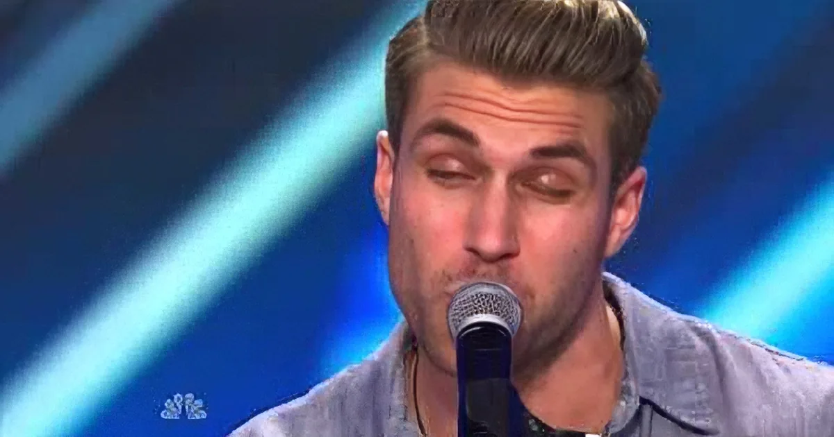A man with short, styled hair sings into a microphone against a blue background.