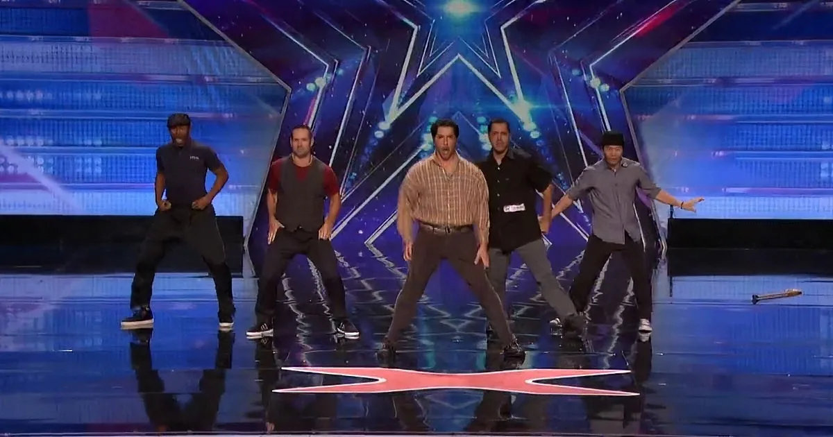Five men in casual attire perform a synchronized dance routine on a stage with a star design.