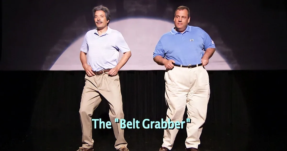 Two men in khaki pants and polo shirts stand on stage, demonstrating a "Belt Grabber" move.