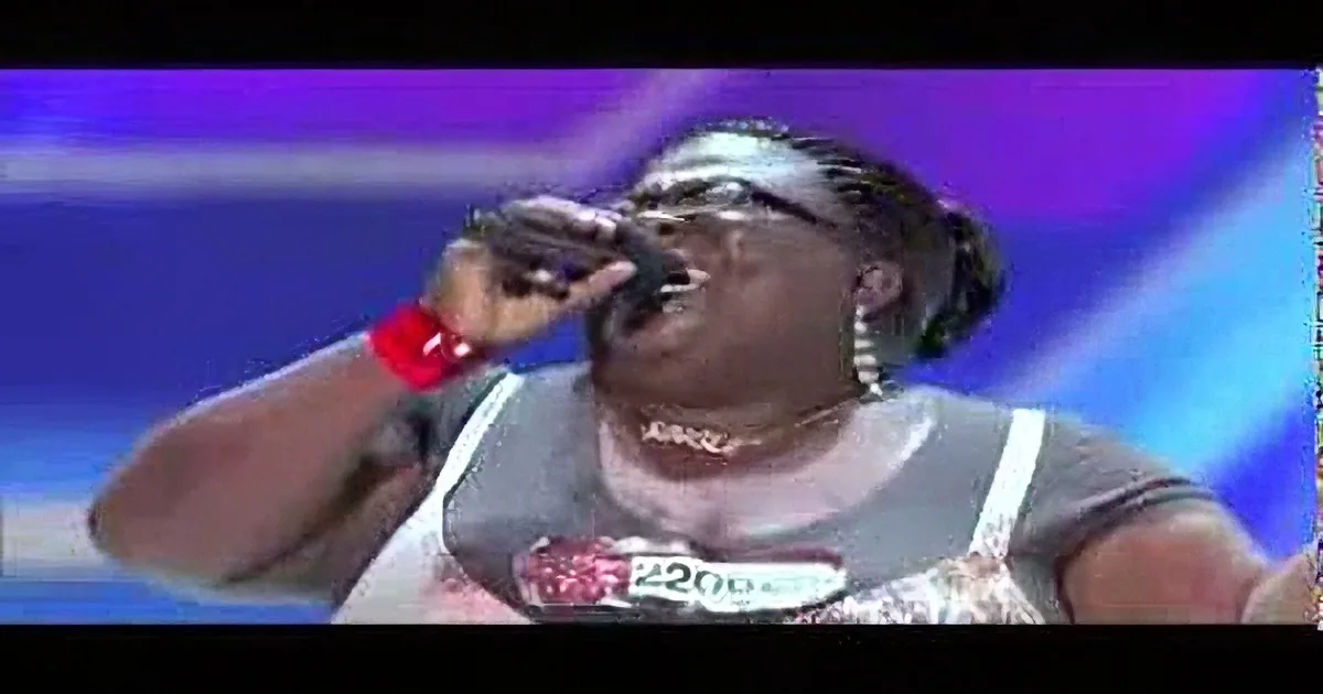 A person wearing a white tank top and red wristband is singing into a microphone.