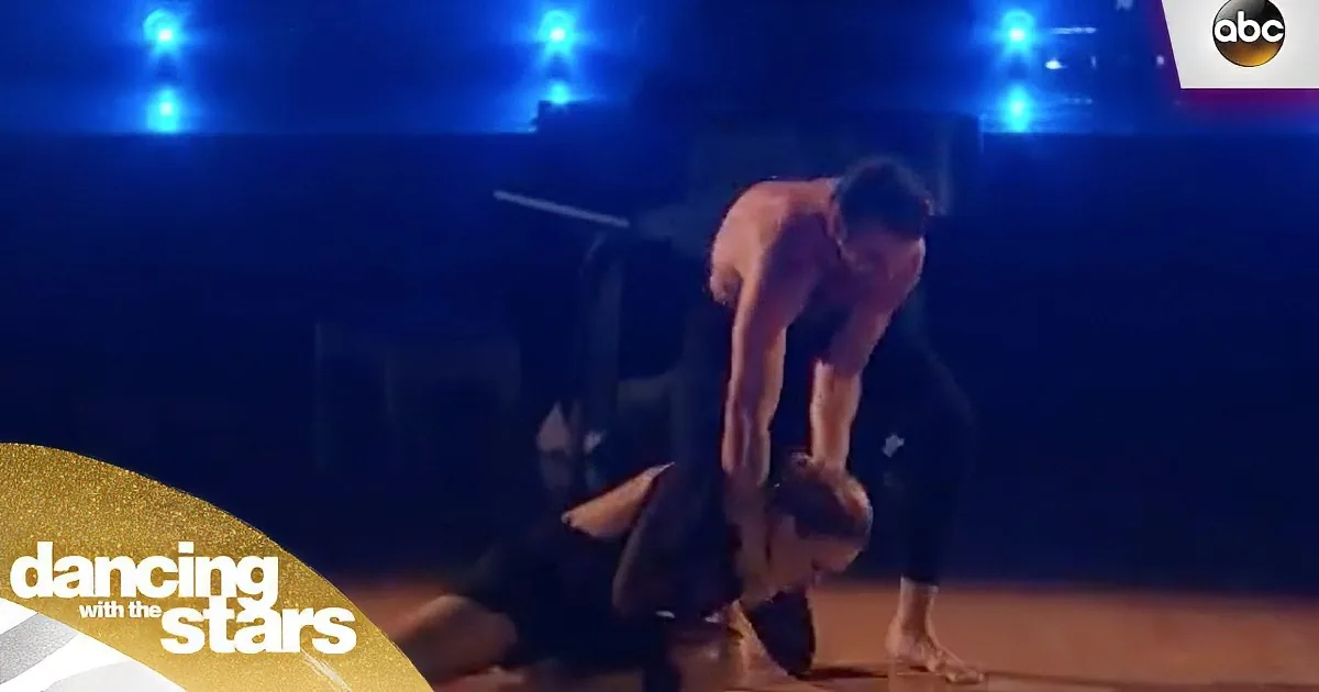 A man leans over another person in a dramatic pose on a stage with blue lights.