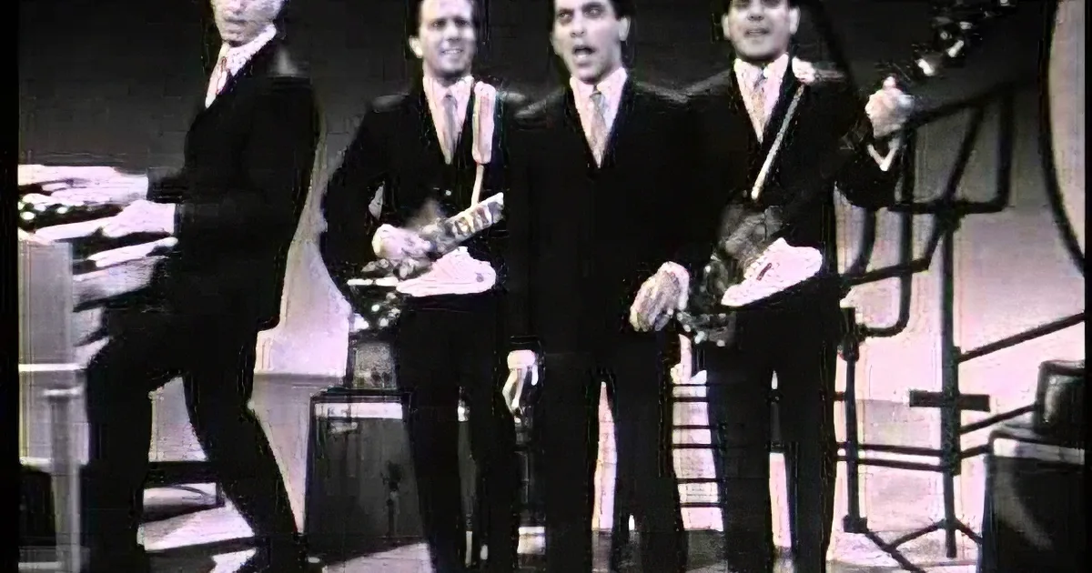 A band in black suits performs on stage, with one member singing and others playing instruments.