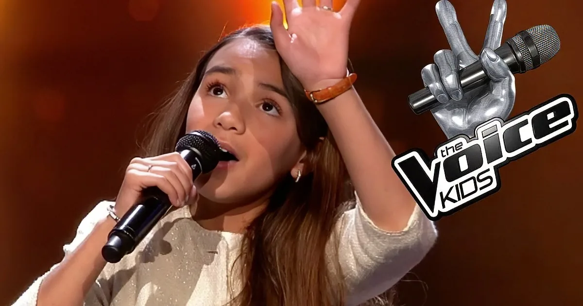 A young singer in "The Voice Kids" holds a microphone, raising her other hand, with a warm stage backdrop.
