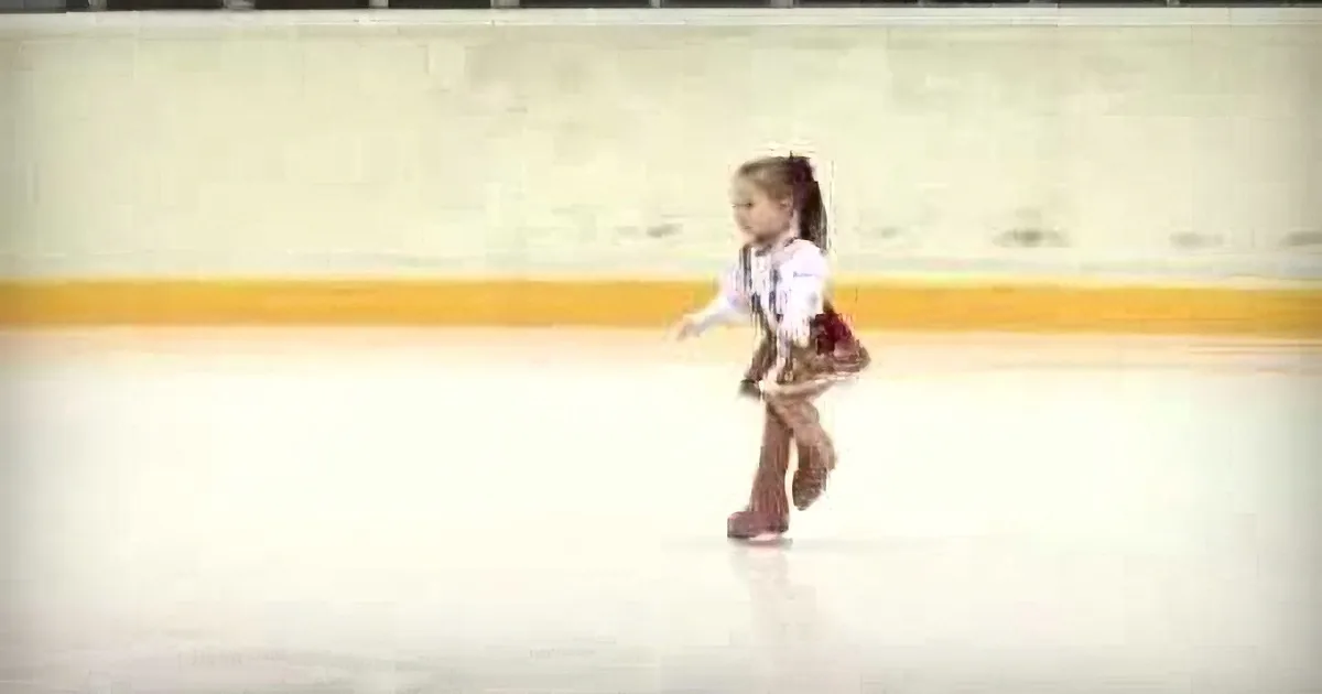 A young girl in a white outfit skates on an ice rink, her arms outstretched.